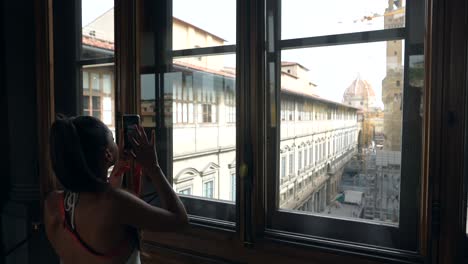 woman taking photo of florence cityscape from a window