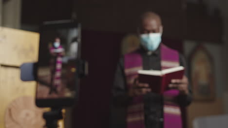 african-american priest wearing mask recording sermon on smartphone