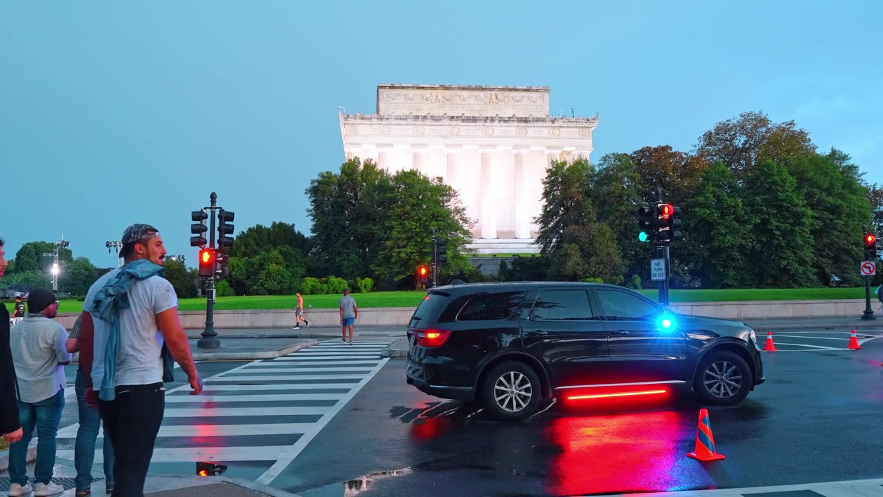 Washington, USA, 13 June 2026: Pedestrians approaching Lincoln Memorial at twilight, Washington D.C. Glowing white facade and columns behind traffic cones, SUV and wet asphalt at blue hour.