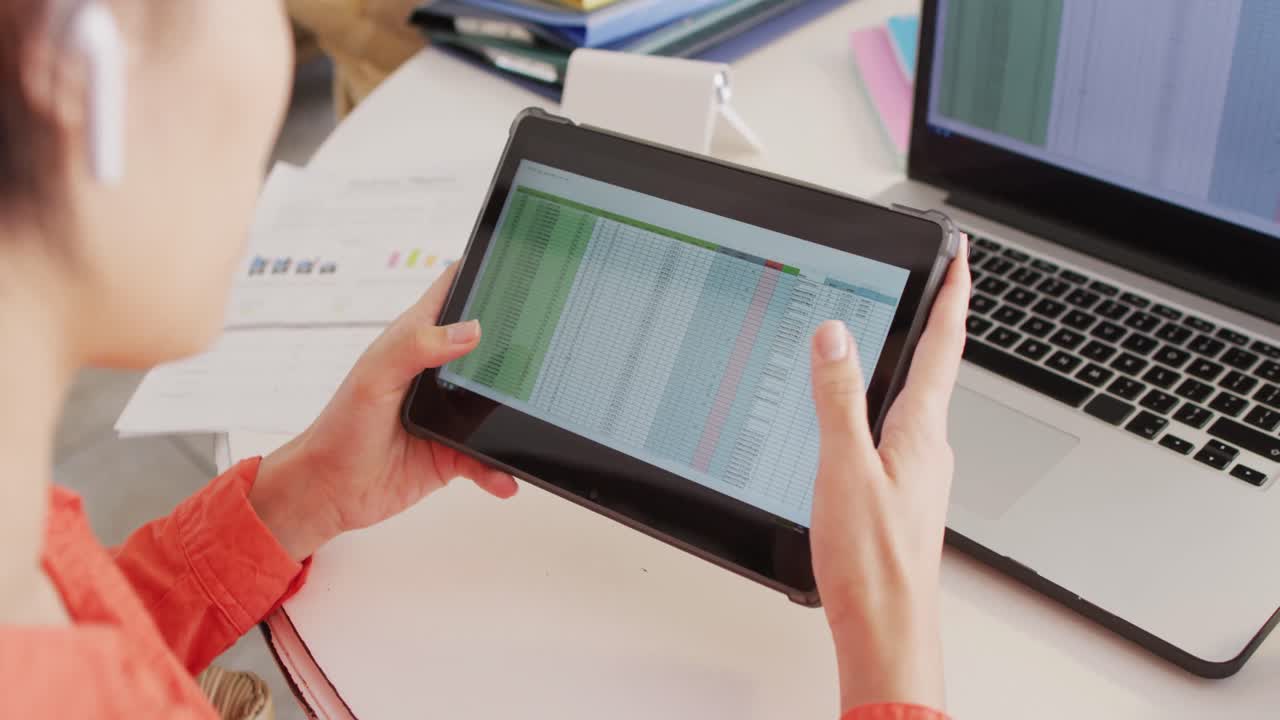 mujer biracial sentada a la mesa y trabajando con una tableta