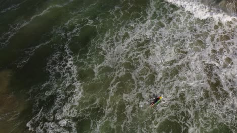 Surfer-paddling-on-colored-surfboards-while-entering-in-Atlantic-Ocean-waters,-La-Pedrera-beach-in-background,-Uruguay