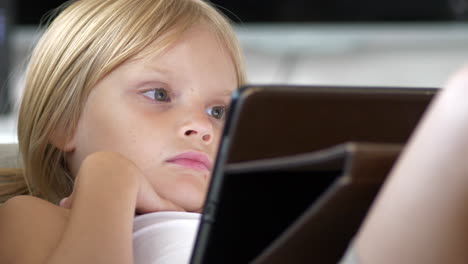 lying blonde little girl relax looking at tablet