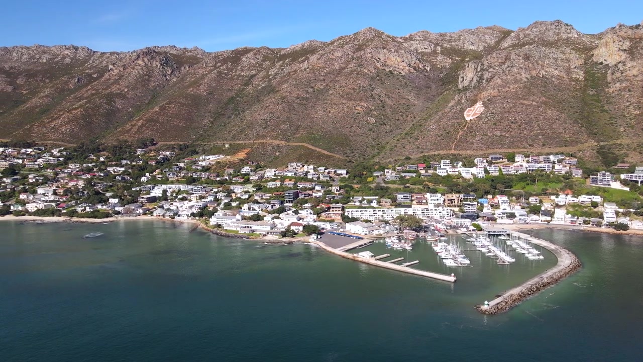 Pueblo costero de Gordon's Bay y puerto deportivo de yates bajo las montañas, vista aérea