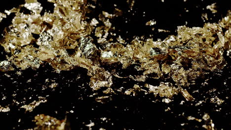 extreme slow motion close-up of chunky gold flakes on black as wind blows it from the right.