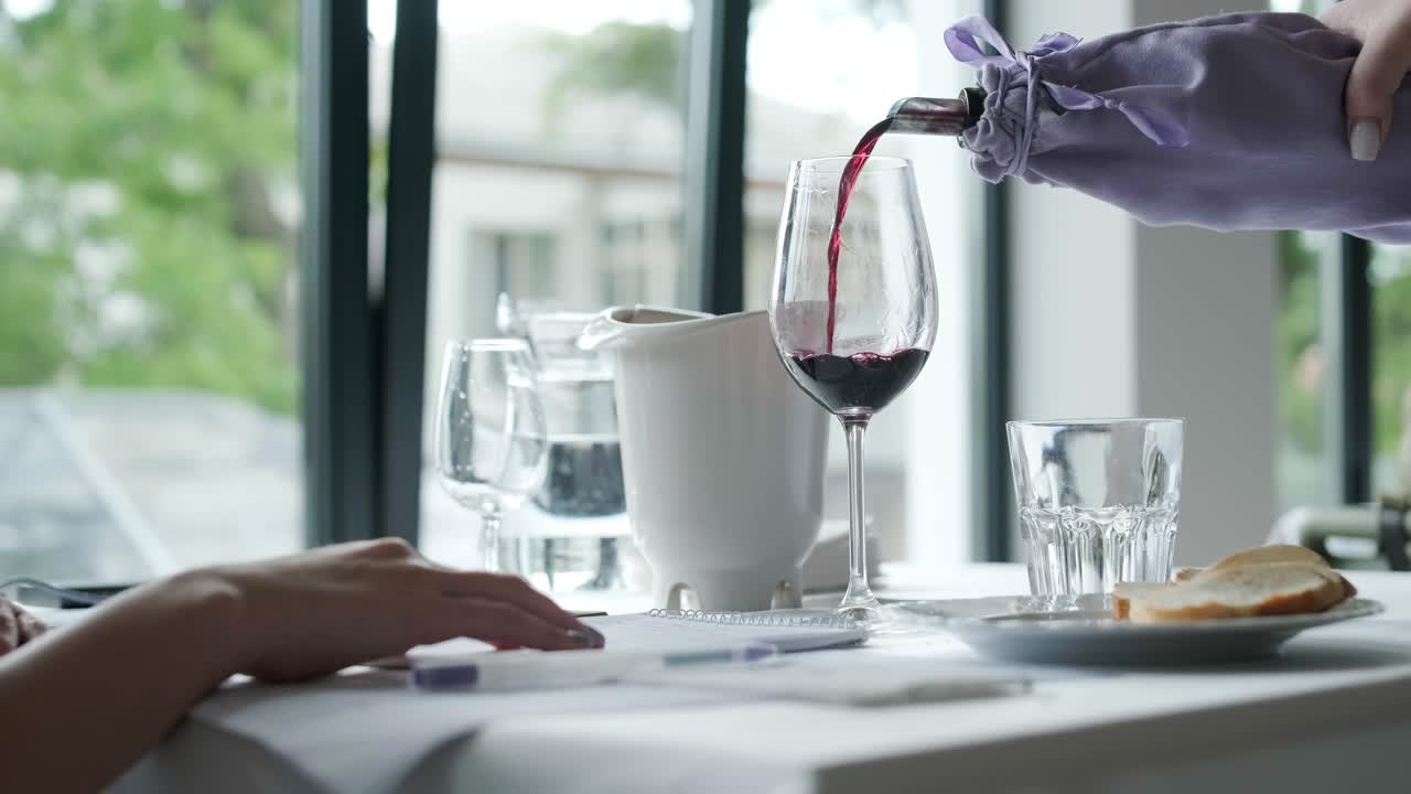 클로즈업: 익명의 웨이터 손이 술잔에 포도주를 고, 젊은 여성 손이 레스토랑 내부에서 음료와 함께 포도주 술잔을 고 있다.