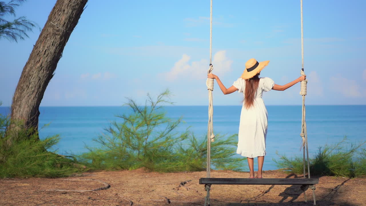 vista trasera de una chica parada en un columpio frente al mar