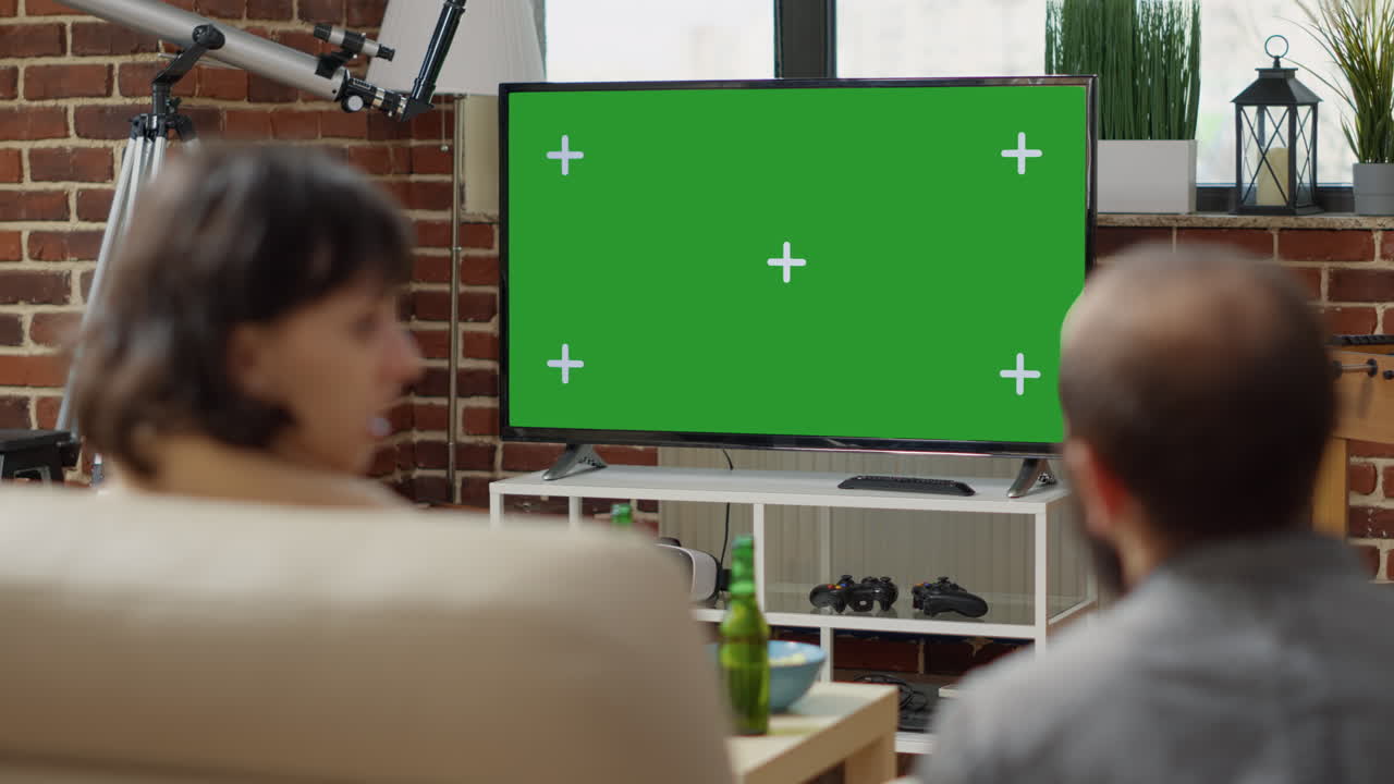 Man and woman watching green screen on television display