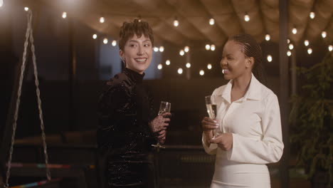 two elegant multiethnic women with champagne glasses talking and laughing at new year's eve party