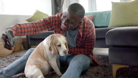 Feliz-Hombre-Afroamericano-Sentado-En-El-Suelo-En-Casa,-Tomando-Selfie-Con-Su-Perro-Mascota,-Cámara-Lenta