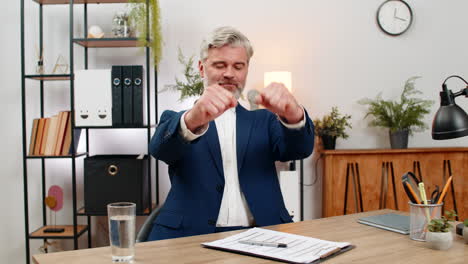Middleaged businessman signs document then dances laughing celebrating project completion triumph