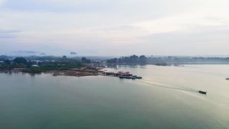 Long-tail-boat-sailing-away-from-jetty-on-hazy-sea-coast-of-Thailand