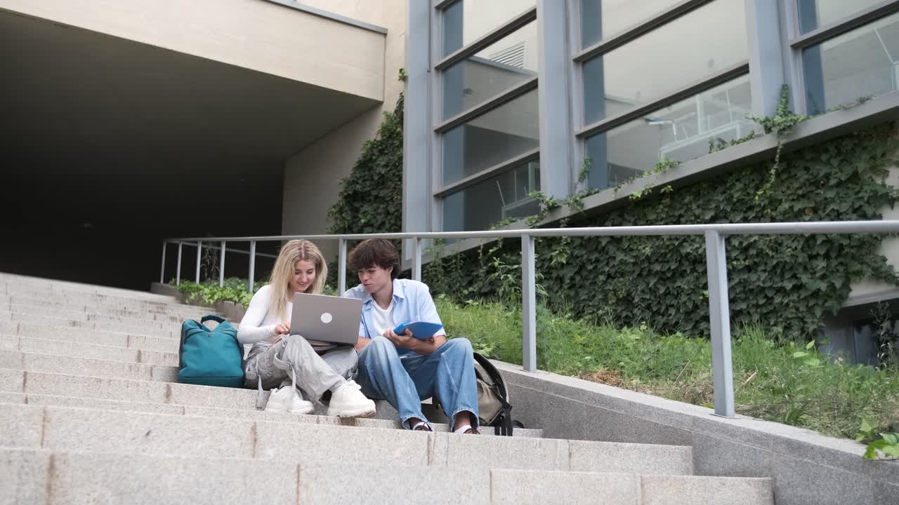 Young friends using netbook on steps outside university building