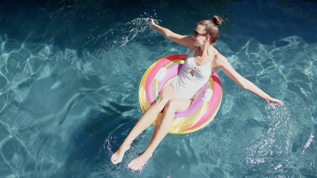 Teenage Caucasian girl enjoys the sun on a colorful float in a pool