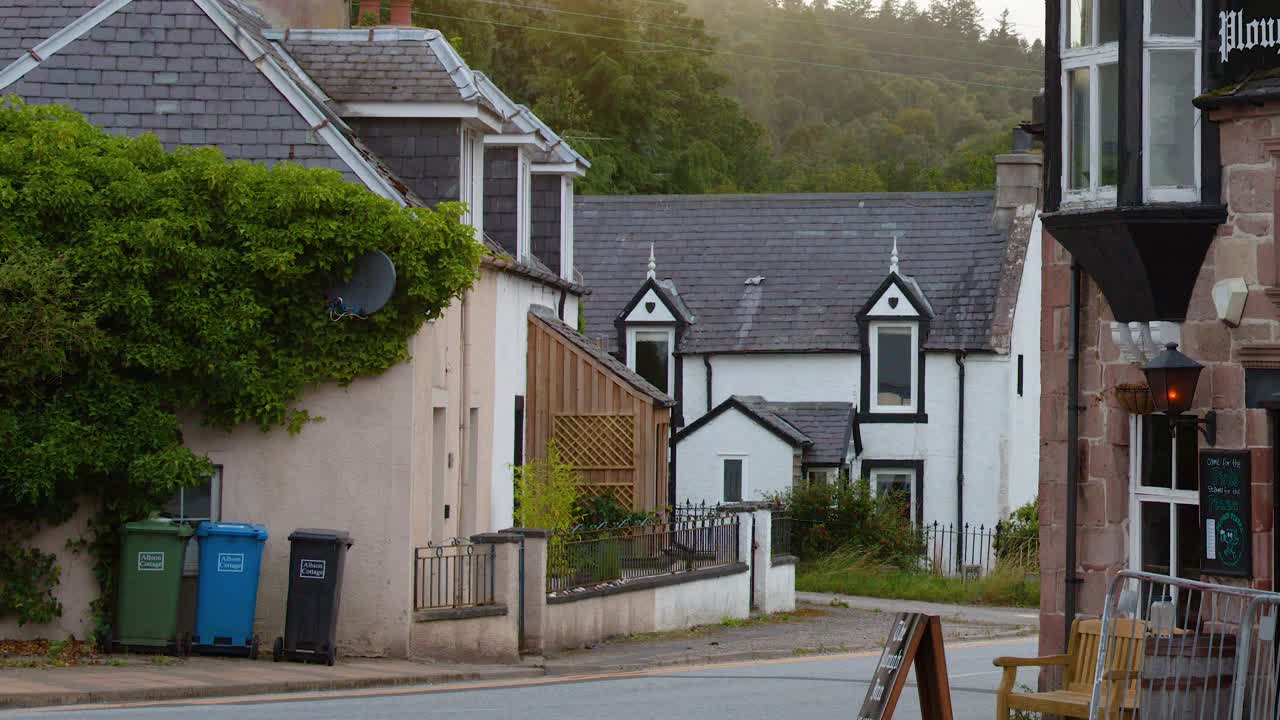 Hvid hatchback-bil passerer traditionelle bygninger på en stille Rosemarkie-gade med overskyet, naturligt lys