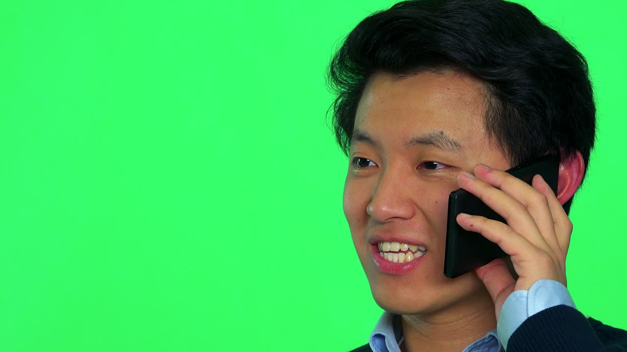 젊은 아시아인 남자가 스마트폰으로 웃으며 이야기합니다. - 그린 스크린 스튜디오 - 클로즈업
