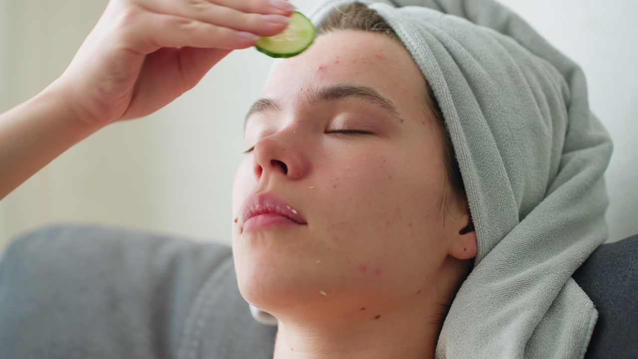 Close-up of woman rubbing cucumber on her forehead as part of a soothing skincare routine, relaxing, rejuvenating moment with natural lighting and towel wrapped around her head
