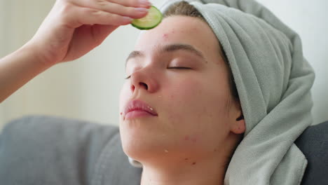 close-up of woman rubbing cucumber on her forehead as part of a soothing skincare routine, relaxing, rejuvenating moment with natural lighting and towel wrapped around her head