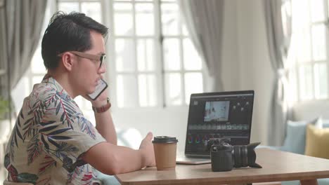 asian man editor talking on mobile phone with video editing app / software on his laptop computer