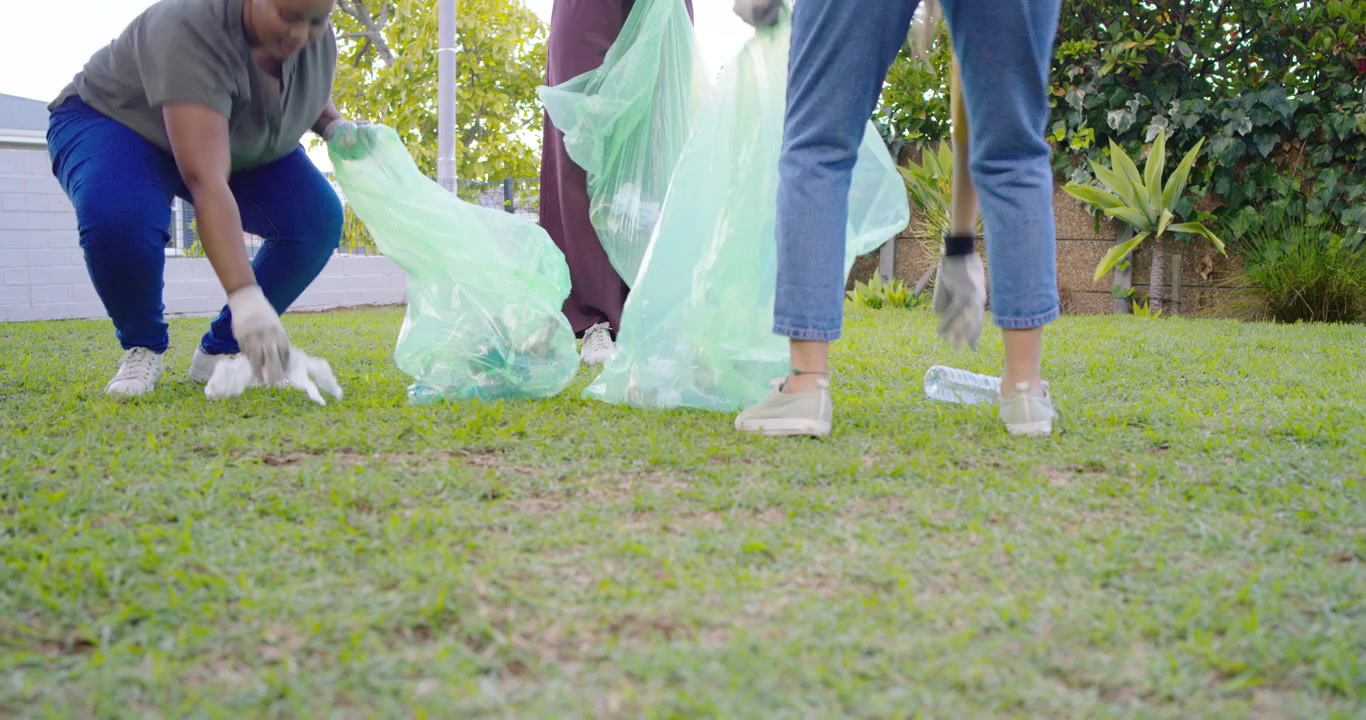 Female volunteers spotting litter wearing gloves picking up bottles into green bags to clean yard