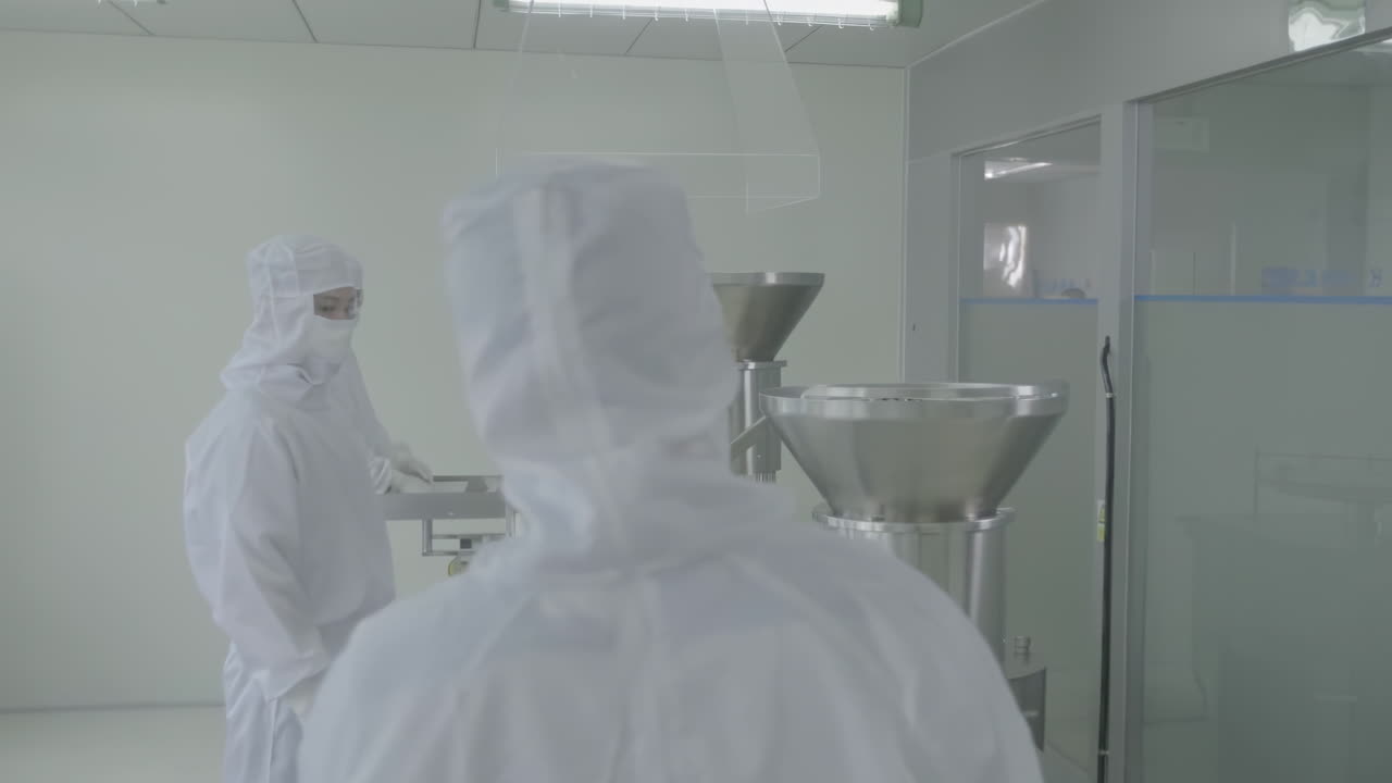 Scientists or technicians in protective gear managing production line at a pharmaceutical manufacturing facility in sterile conditions