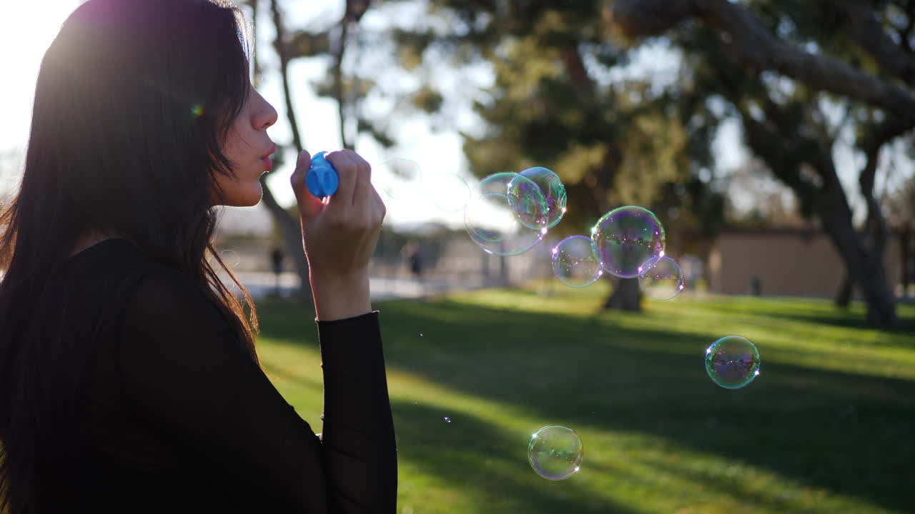 Beautiful young woman blowing bubbles floating in dreamy sunshine and lens flares outdoors at sunset SLOW MOTION