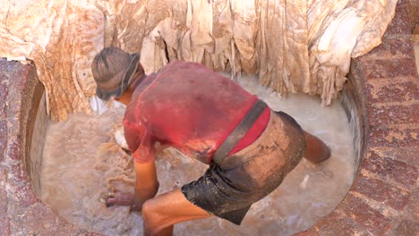 un hombre lavando el cuero en una curtiduría en fez, con las piernas dentro del agua sucia