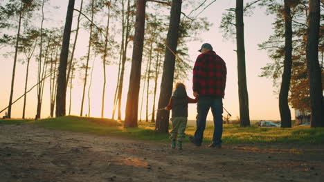 old fisher and his little grandson are going to fish in lake in forest walking together in beautiful landscape