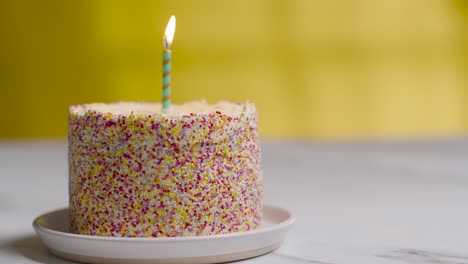 Single-Candle-Being-Blown-Out-In-Studio-Shot-Of-Birthday-Cake-Covered-With-Decorations-3