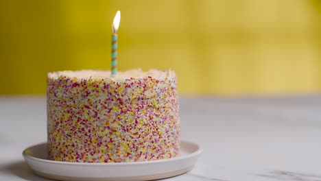 single candle being blown out in studio shot of birthday cake covered with decorations 3