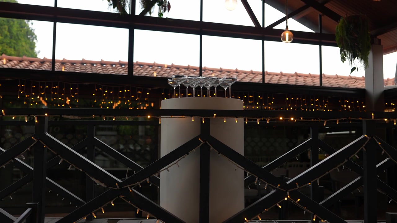 Elegantes copas de champán dispuestas en un soporte, listas para un brindis en un evento de celebración con guirnaldas de luces brillantes.