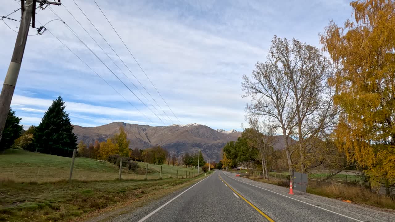 A serene drive through New Zealand's countryside in autumn, showcasing vibrant foliage and mountainous landscapes under a clear sky