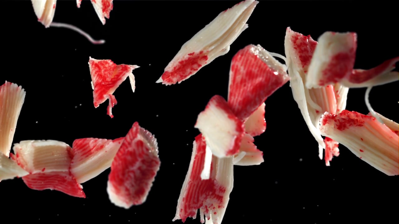 Pieces of Crab Stick Falling in Slow Motion Against Black Background