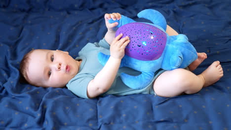 beautiful caucasian baby boy lies on back holding a toy turtle. kid smiling sweetly and banging by his toy cheerfully. side view.