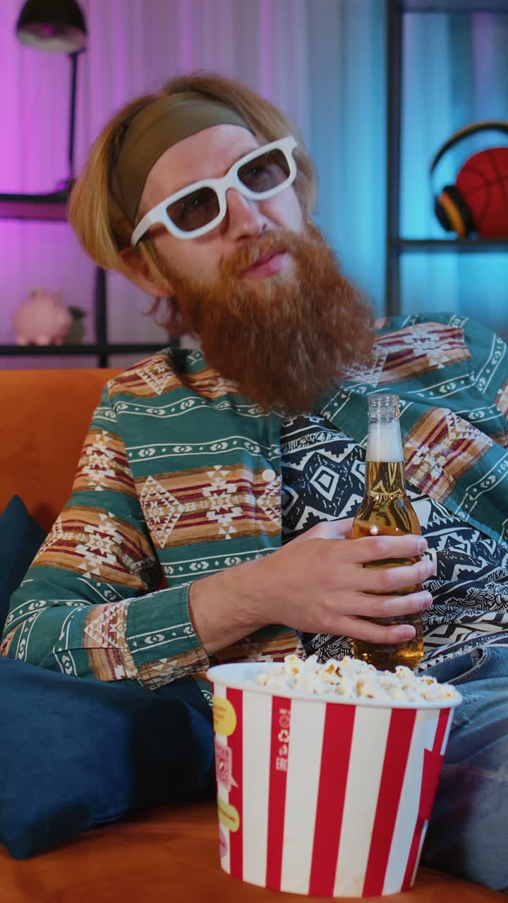 Man sitting on couch eating popcorn and watching interesting tv serial sport game online at home