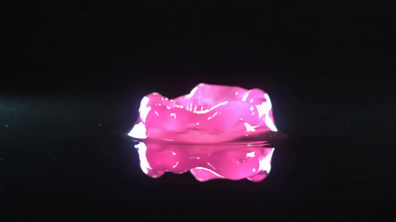Striking pink droplet forming crown and column on mirror surface, under studio lighting