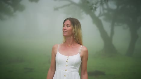 Attractive-blond-woman-in-white-dress-looking-amazed-in-misty-forest