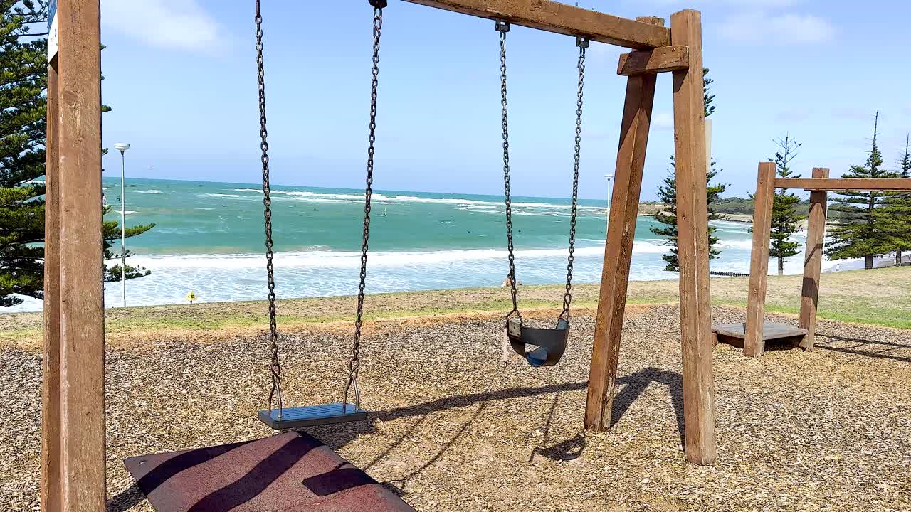 Wooden swings stand still by the ocean in Torquay, Australia. Bright daylight highlights the serene coastal setting