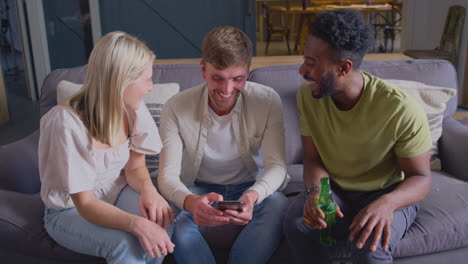 Amigos-Multiculturales-Sentados-En-El-Sofá-Del-Salón-De-Casa-Mirando-Juntos-El-Teléfono-Móvil