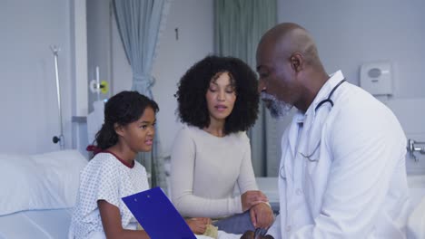 African-american-senior-male-doctor-with-clipboard-talking-to-mother-and-daughter-at-hospital