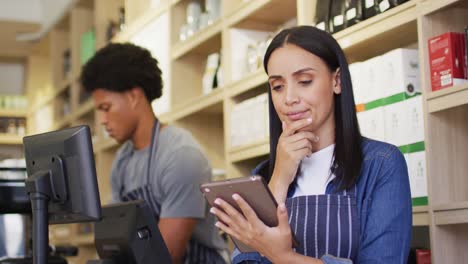 animation of thoughtful biracial waitress using tablet in coffee shop