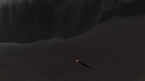 tropical beach aerial bird eye view of volcanic black sand and foaming ocean waves, man lying on the beach walking towards the ocean. bollullo beach, tenerife