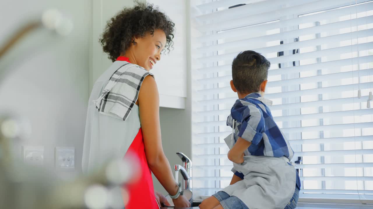madre negra con su hijo lavando los platos en la cocina en casa 4k