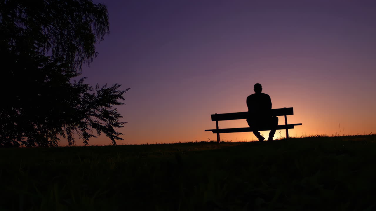 Silhouette di una persona seduta su una panchina al tramonto