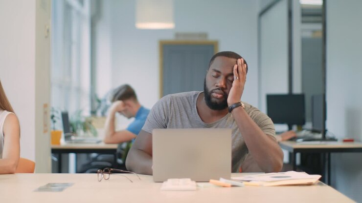 Sleepy man sleeping at workplace. Slipping man rubbing eyes at open space.