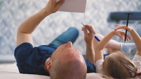 father daughter do home assignment together lying on floor