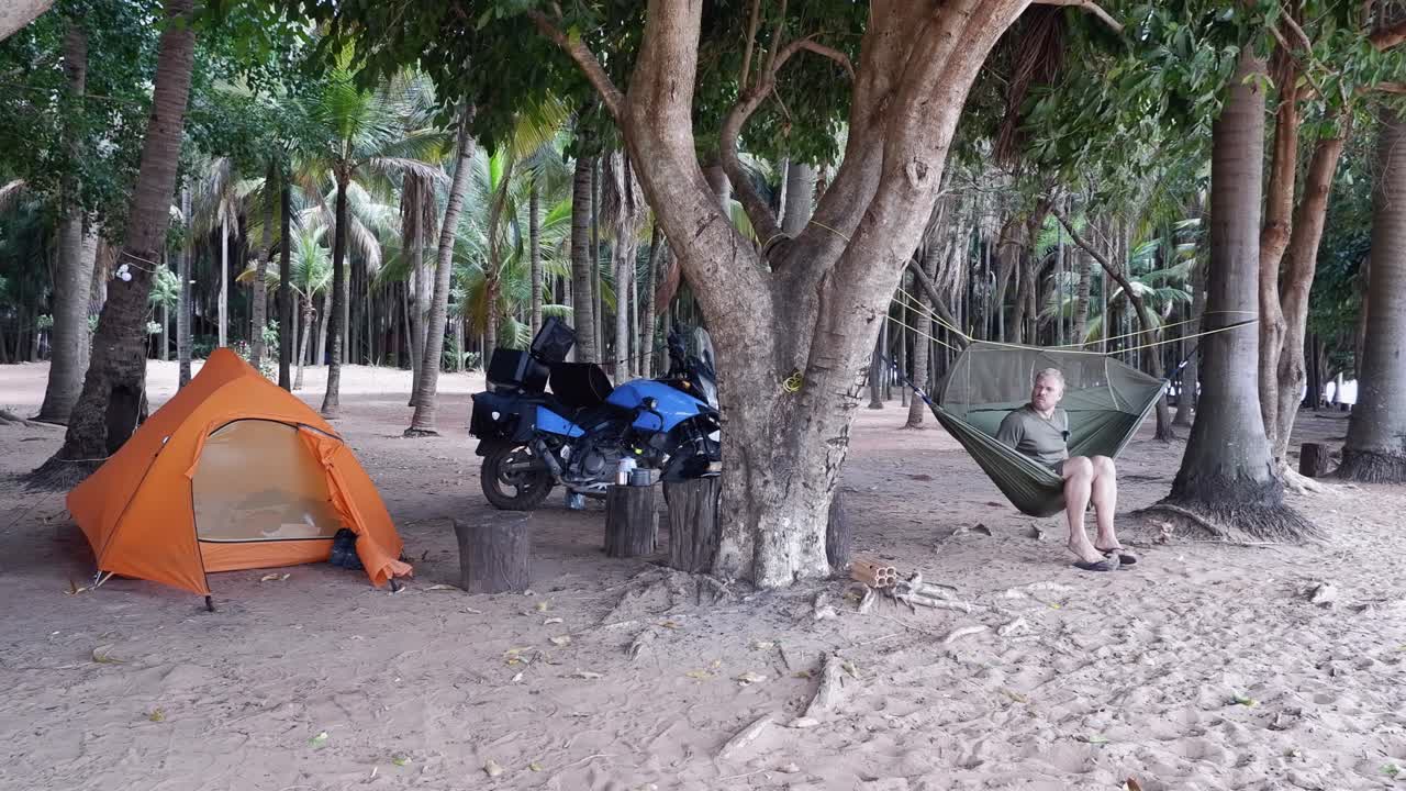 Caucasian male traveller at tropical beach campsite gets into hammock