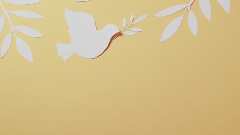 Close-up-of-white-dove-with-leaves-and-copy-space-on-yellow-background
