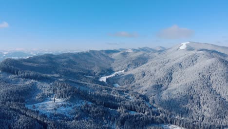 scenic view of snowy mountains with pine trees against blue cloudy sky - aerial drone shot