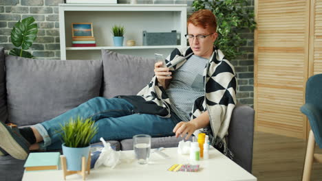 sick man on couch with phone and medicine