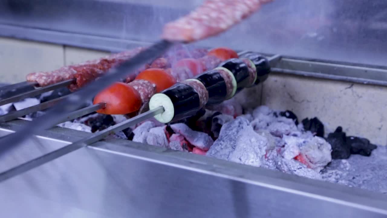 A chef puts a set of kebabs skewers on a burning coal stove and smoke rises from it
